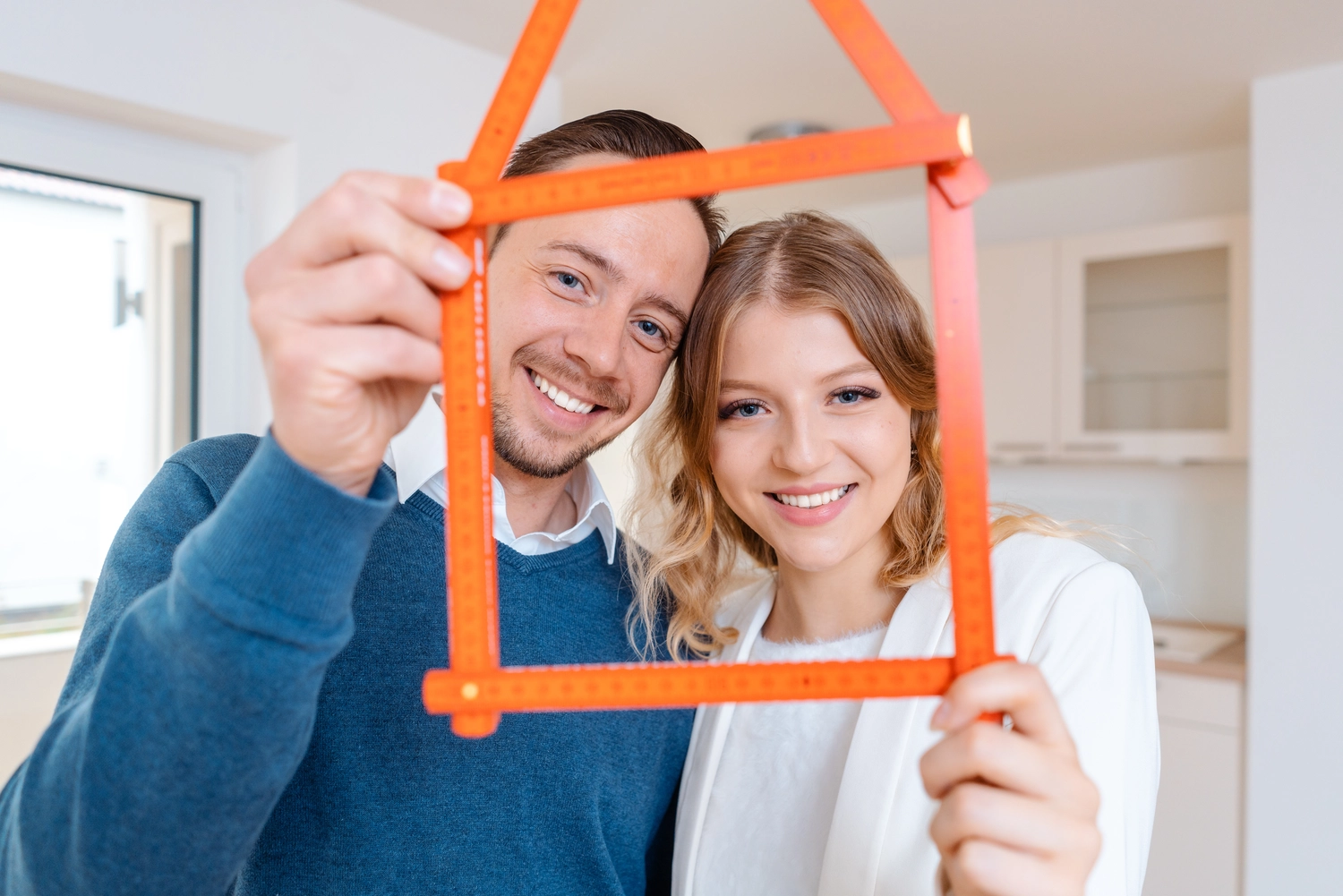 K | S Immobilien – glückliches Paar mit einem Hausmodell aus orangefarbenen Eisstielen in den Händen